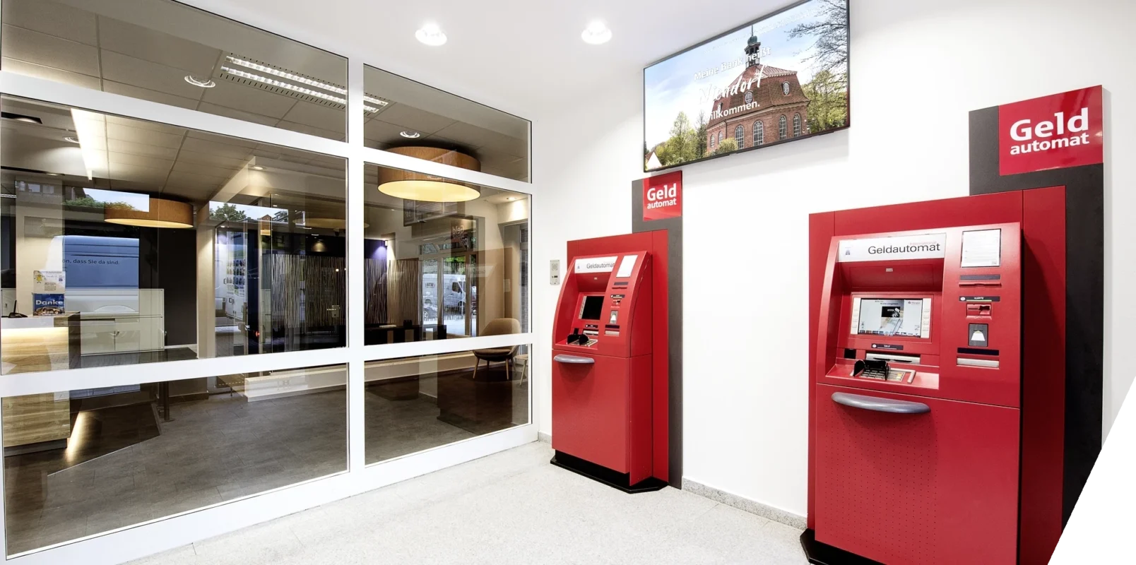 In a Haspa branch, there are two ATMs. Above them, a screen displays local content.