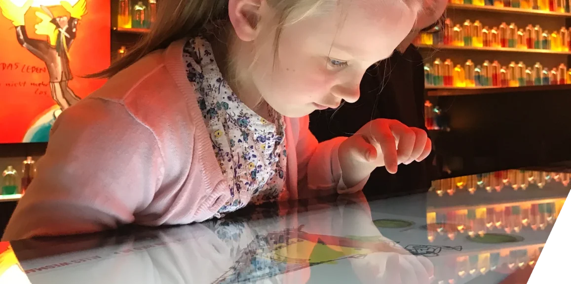 A girl is looking intently at an interactive touch table in Panik City, where she is digitally coloring something.