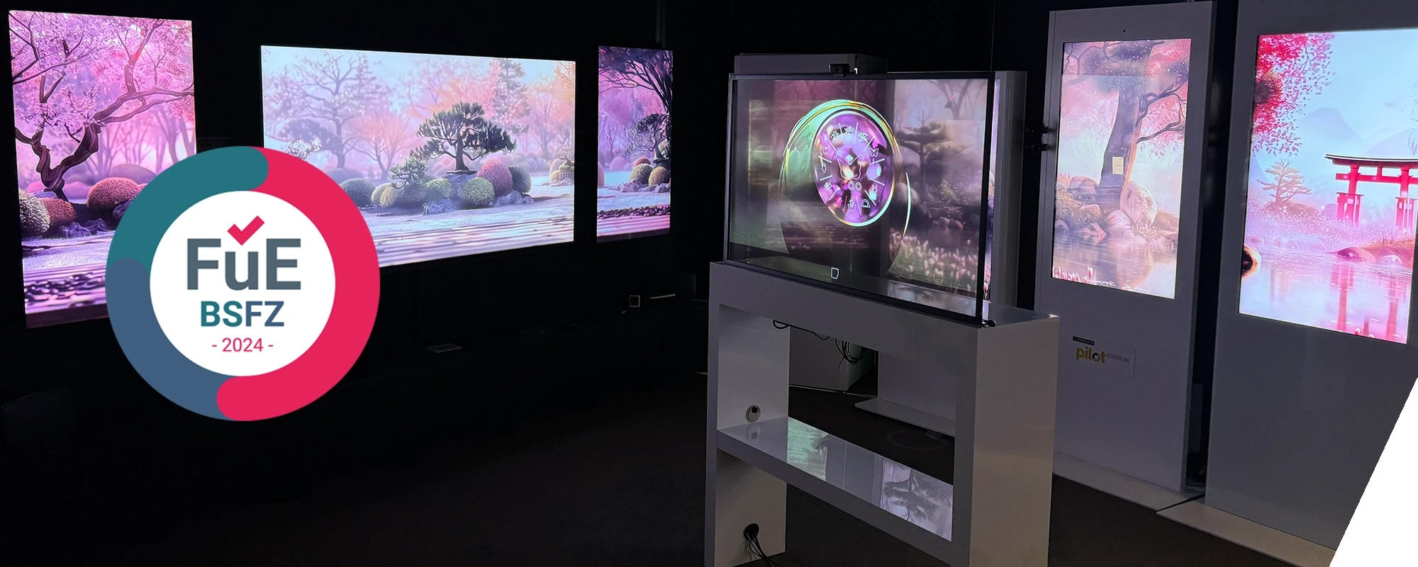 Man sieht das BSFZ Siegel, welches eine Auszeichnung für Innovation ist vor einem Showroom mit verschiedenen Bildschirmen angezeigt wird.